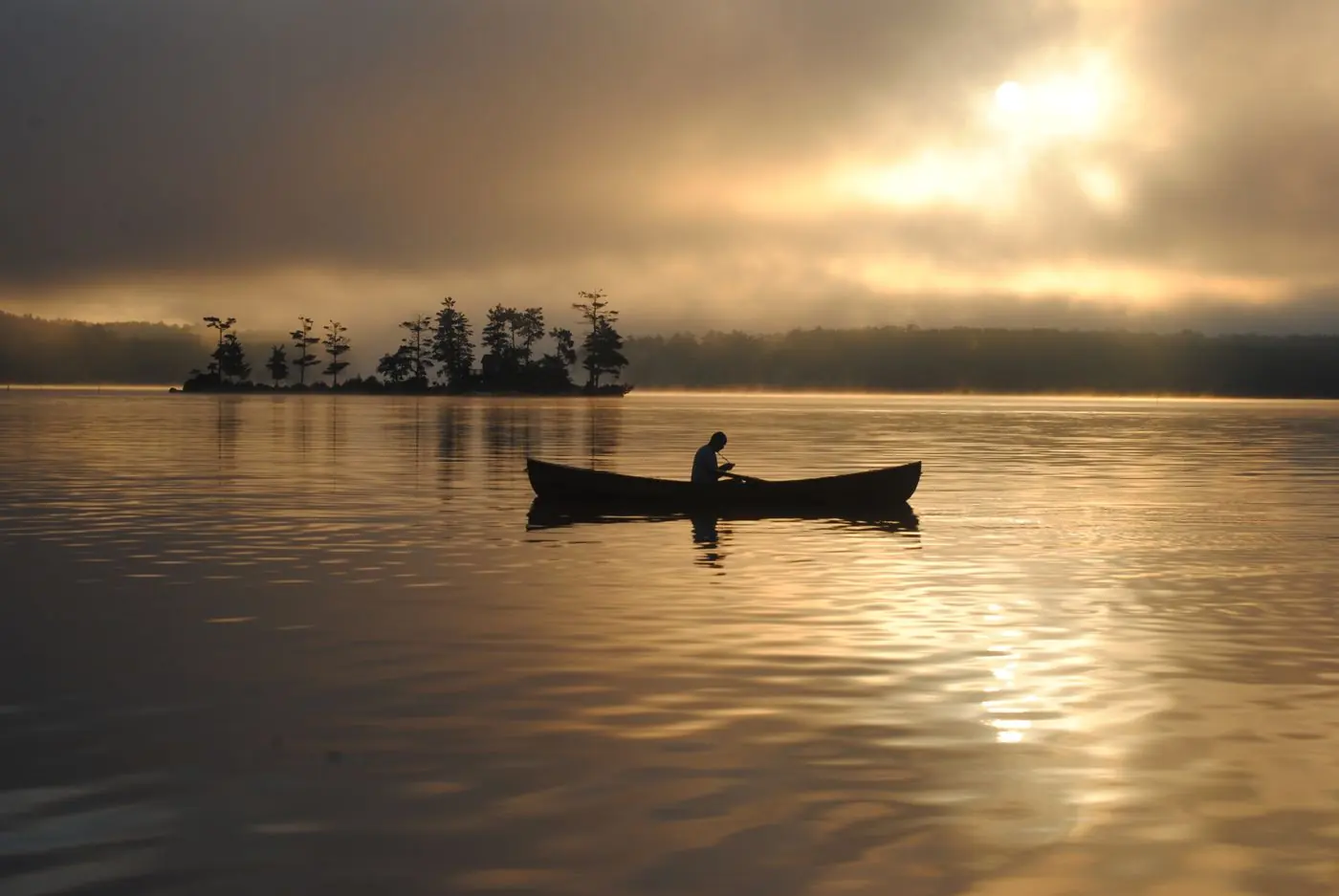 A canoe gliding across a misty lake at sunrise